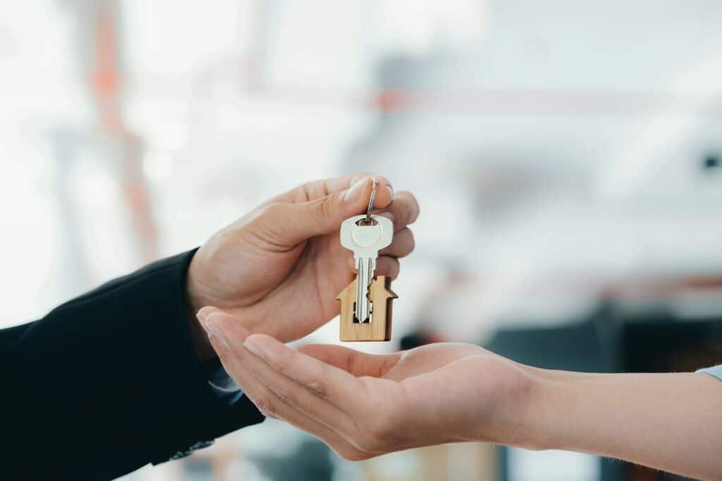 Close-up Of Real Estate Agent Giving Key To Client In Front Of House